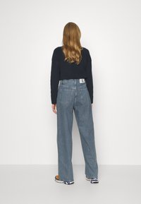 Laineet siniset farkut leveillä lahkeilla ja korkealla vyötäröllä, joissa on takataskut ja merkkikohtainen nahkalappu. Yhdistettynä lyhytmalliseen mustaan neulepuseroon.