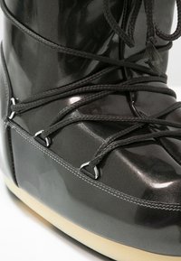 Gros plan sur une botte d'hiver gris foncé brillante avec une semelle épaisse beige et des lacets noirs passés dans des œillets en métal.