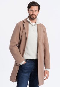 Abrigo de mezcla de lana marrón con silueta ajustada, diseño de un solo botón, dos botones y bolsillos laterales, superpuesto a un suéter de punto blanco.