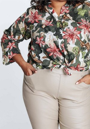 Bluzka w kwiatowy wzór, z krótkim rękawem, w kolorach zielonym, białym i czerwonym; zawiązana w talii na supeł. Do tego dopasowane, jasnobeżowe spodnie z kieszeniami.