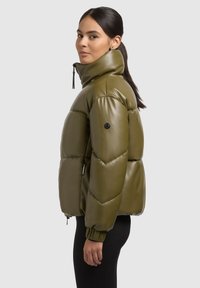 Olive green puffer jacket with a high collar, glossy finish, quilted design, elastic cuffs, and side pockets. Black logo on the sleeve.