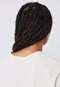 Capelli intrecciati che passano dal nero al marrone, visti da dietro, con una t-shirt chiara che presenta un delicato dettaglio a stella vicino al colletto.