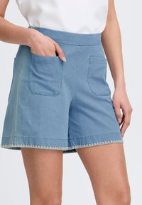 Shorts de mezclilla en azul claro con una cintura alta, dos bolsillos frontales y un dobladillo en forma de ola. Textura suave y diseño casual.