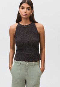 Mörkgrå virkade halterneck-top med texturerat mönster och vågig fåll, kombinerad med ljusgröna högmidjade byxor.