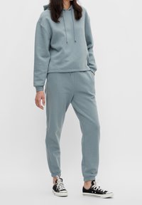 Set di felpa e pantaloni tuta azzurro chiaro realizzato in morbido cotone. Presenta una tasca frontale, cappuccio con lacci e polsini elasticizzati. Abbinato a sneaker nere.