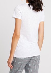 Bílá krátkozávěsá tričko s texturovaným vzorem, spárované s kalhotami s kostkovaným vzorem, s volným střihem a kulatým výstřihem.