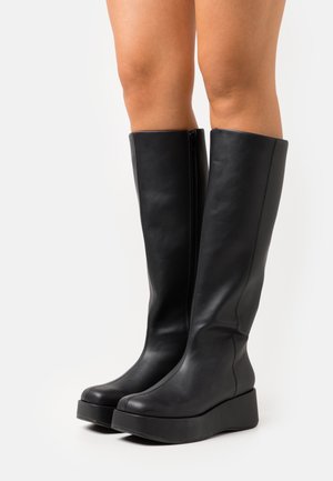 Stivali neri al ginocchio realizzati in pelle liscia con una suola platform spessa e zip laterale. Design semplice e moderno senza motivi visibili.