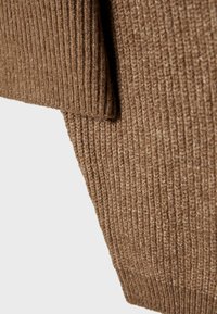 Gros plan sur un tissu en maille côtelée marron montrant la texture détaillée et les coutures sur une manche et une partie du corps.