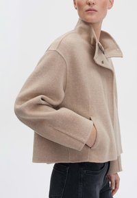 Beige wol-mix cropped jas met een hoge kraag, knoopsluiting en zijzakken. Zachte textuur en een relaxte pasvorm.