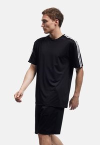 Schwarzes Sporttrikot und Shorts aus glattem, leichtem Stoff. Das Trikot hat weiße Streifen auf den Schultern. Gerader Schnitt.