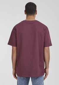 Burgundy színű pamut póló rövid ujjakkal, kerek nyakkivágással és laza fazonnal. Simább textúrájú, látható minták nélkül, sima hátoldali nézettel.