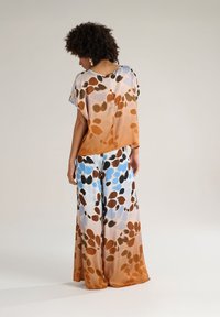 Completo in seta leggero e fluido composto da una blusa e pantaloni a gamba larga. Il design presenta un motivo floreale multicolore in tonalità terrose.