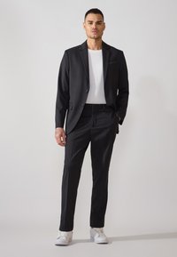 Costum negru cu un design slim-fit, sacou cu un singur nasture și pantaloni drepți; asortat cu un tricou alb și adidași albi.