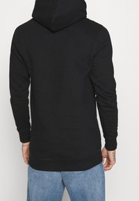 Felpa nera con cappuccio regolabile e maniche lunghe, caratterizzata da una texture liscia e una vestibilità comoda, abbinata a jeans azzurri chiari.