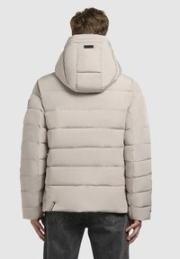 Svetlo bež puffer jakna z oblazinjenjem, ki ima snemljivo kapuco, ravno rez in rebraste detajle na rokavih.