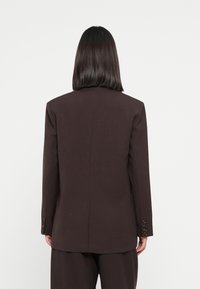 Brauner maßgeschneiderter Blazer mit strukturierter Silhouette, Spitzkragen und Knopfmanschetten. Glattes Material, minimale Details, rückseitige Belüftung für besseren Sitz.