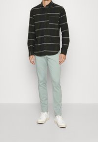 Zwart-en-groen gestreepte flanellen shirt met een borstzak, gecombineerd met lichte mintgroene broek en witte sneakers.