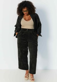 Zwarte veloursbroek met een losse pasvorm, hoge taille, plooien en zijzakken, gecombineerd met een beige tanktop en een bijpassend oversized overhemd met knopen.