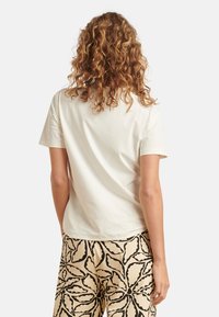 Lichtbeige, kortärmige t-shirt van zacht stof, met een eenvoudig ontwerp, een ronde halslijn en een relaxte pasvorm. Achteraanzicht weergegeven.