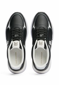 Schwarze Sneaker aus synthetischem Leder mit weißen Akzenten, featuring eine strukturierte Oberfläche, Schnürung und ein Logo auf der Zunge und an der Seite.