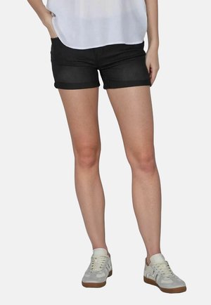 Pantalones cortos de mezclilla negros con mangas enrolladas, combinados con zapatillas blancas con acentos gris clarito y superficie texturizada. Diseño sencillo, ajuste natural.