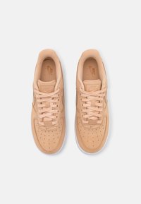 Tan lädersneakers med perforeringar för andningsförmåga, platta snörningar och en vit gummisula. Har diskret branding på tungan.