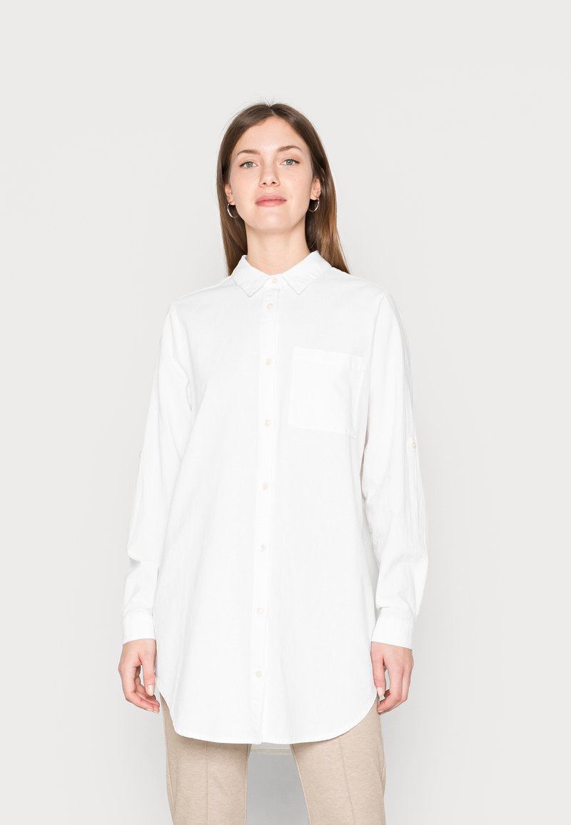Camisa branca de botões, feita de tecido texturizado, com colarinho, mangas longas, um bolso no peito e uma bainha arredondada.