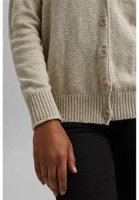Cardigan beige lavorato a maglia con polsini a coste e chiusura con bottoni. Realizzato in un tessuto morbido e testurizzato, con variazioni di colore sottili.