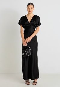 Μαύρο μακρύ φόρεμα από σατέν με V-λαιμόκοψη, κοντά φουσκωτά μανίκια και εφαρμοστή σιλουέτα. Συνδυασμένο με μικρή μαύρη τσάντα με καρφιά και σανδάλια με λουράκια.