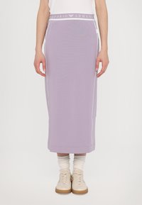 Lilac midi sijonas su baltu elastingu juosmeniu, ant kurio yra "Emporio Armani" logotipas. Lygus audinys, šoninės siūlės detalės, sujungtas su smėlio spalvos sportbačiais.