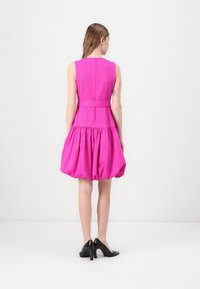 Růžové šaty bez rukávů s přiléhavým trupem a rozšířeným, řaseným lemem. Obsahují zip na zadní straně a pásek v oblasti pasu.