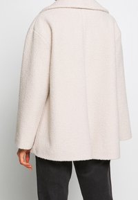 Chaqueta de gran tamaño de color beige claro, hecha de un tejido texturizado. Presenta un cuello ancho y hombros caídos, con un corte relajado y un dobladillo recto.