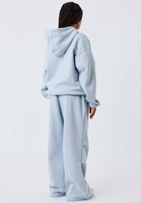 Haut de hoodie surdimensionné bleu clair avec capuche, poignets côtelés et pantalon de jogging ample assorti en tissu doux et texturé. Design minimaliste.