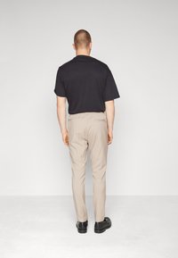 Svart t-shirt med kort ärm i kombination med ljusbeiga byxor och svarta skor. Byxorna har en bakficka och en jämn textur genom hela plagget.