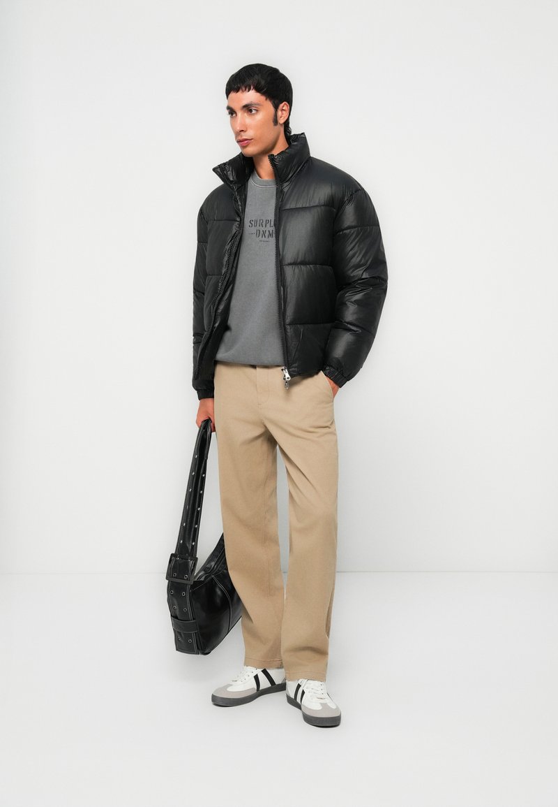 Czarna puchówka, szary sweter z napisem, beżowe spodnie, czarna torba i trampki z szarymi podeszwami. Gładkie tekstury z eleganckim designem.