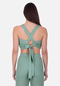 Grøn cropped top med et struktureret, vævet design. Har brede, krydsede stropper og en bundet sløjfe bagpå.