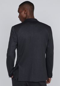 Chaqueta de traje gris oscuro con solapa de muesca, única abertura en la parte posterior y textura sutil. Presenta un corte ajustado y detalles de diseño elegantes.