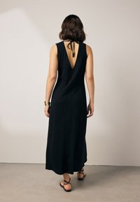 Zwarte maxi-jurk met een diepe V-rug, mouwloos ontwerp, gemaakt van zachte stof, met een strikdetail bij de halslijn en een vloeiende silhouet.
