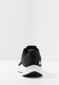 Zwarte sportieve schoen met een slank ontwerp, bovenwerk van textuurstof, witte tussenzool en kenmerkend Swoosh-logo op de hiel.