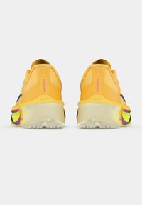 Gule joggesko med lilla detaljer, en polstret såle og teksturert bunn for grep. Merkevare synlig på hælen.