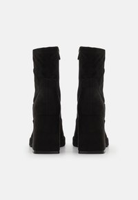 Bottes basses en daim noir avec un talon épais, présentant une texture lisse et un détail de fermeture éclair latérale, conçues pour une silhouette ajustée et profilée.