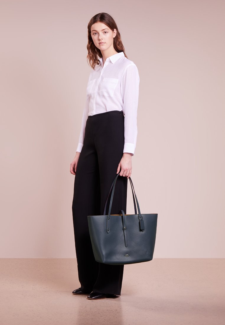 Bolso tote de cuero verde oscuro con dos asas, textura suave, forma rectangular y detalles de hardware sutiles. Sin patrones visibles.