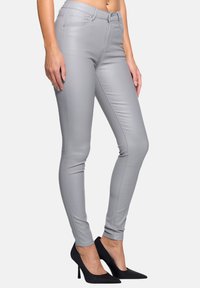 Graue Skinny-Jeans aus Kunstleder mit fünf Taschen, sichtbaren Nähten und einem Reißverschluss, kombiniert mit schwarzen High-Heels.