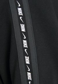Tejido negro con rayas verticales en negro y gris que presentan el texto de Nike en blanco y logotipos del swoosh repetidos.