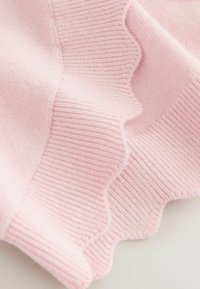 Vaaleanpunainen neulottu kangas, jossa on resorimainen rakenne ja aaltoileva reunus, esittelee pehmeitä, sileitä kuituja ja tasaisen sävyn.