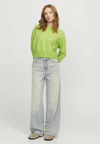 Limonengrüner, verkürzter Pullover mit rippenförmigem Saum, kombiniert mit hellblauen, weiten Jeans und grauen Slippern. Glatte Textur überall.