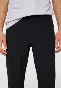 Czarne, lekkie spodnie o dopasowanym kroju, z bocznymi kieszeniami, gładką teksturą i minimalistycznym designem, bez widocznych znaków firmowych.