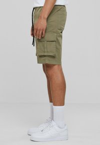 Olive green cargo shorts with multiple pockets, drawstring waistband, and lightweight fabric. Worn with white sneakers and socks.