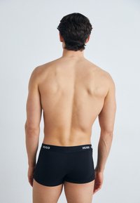 Schwarze Boxershorts mit einem weißen Logo-Bund, taillierte Passform, glatte Textur und niedriger Schnitt, von hinten betrachtet.