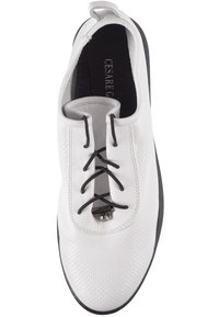 Zapato blanco perforado con cordones negros y un pequeño acento metálico; cuenta con una puntera redondeada y una suela texturizada para mayor agarre.